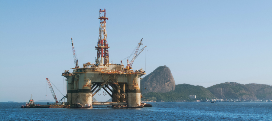 An offshore oil rig is pictured on the water with a landscape of hills in the background.